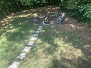 Relax in a peaceful retreat surrounded by lush greenery, with a fire pit at the center of this serene outdoor seating area.