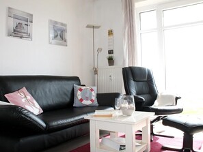 A modern living room with a black leather sofa, a white coffee table, and a black office chair.