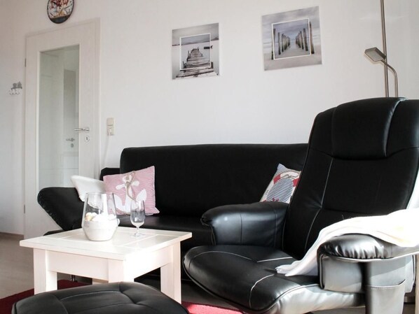 A living room with a black leather sofa, a white coffee table, and two framed pictures on the wall.