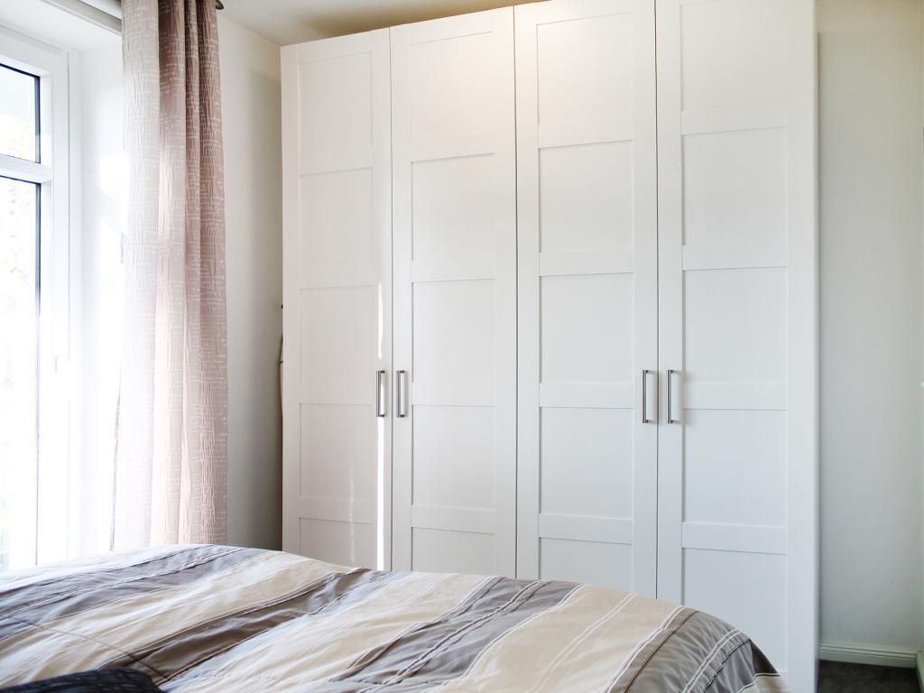 Et soveværelse med en seng, et vindue med gardiner og en hvid garderobe med to døre.