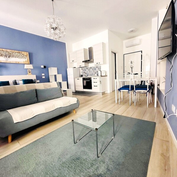 A modern living room with a sofa, a glass coffee table, and a dining area with chairs and a table.