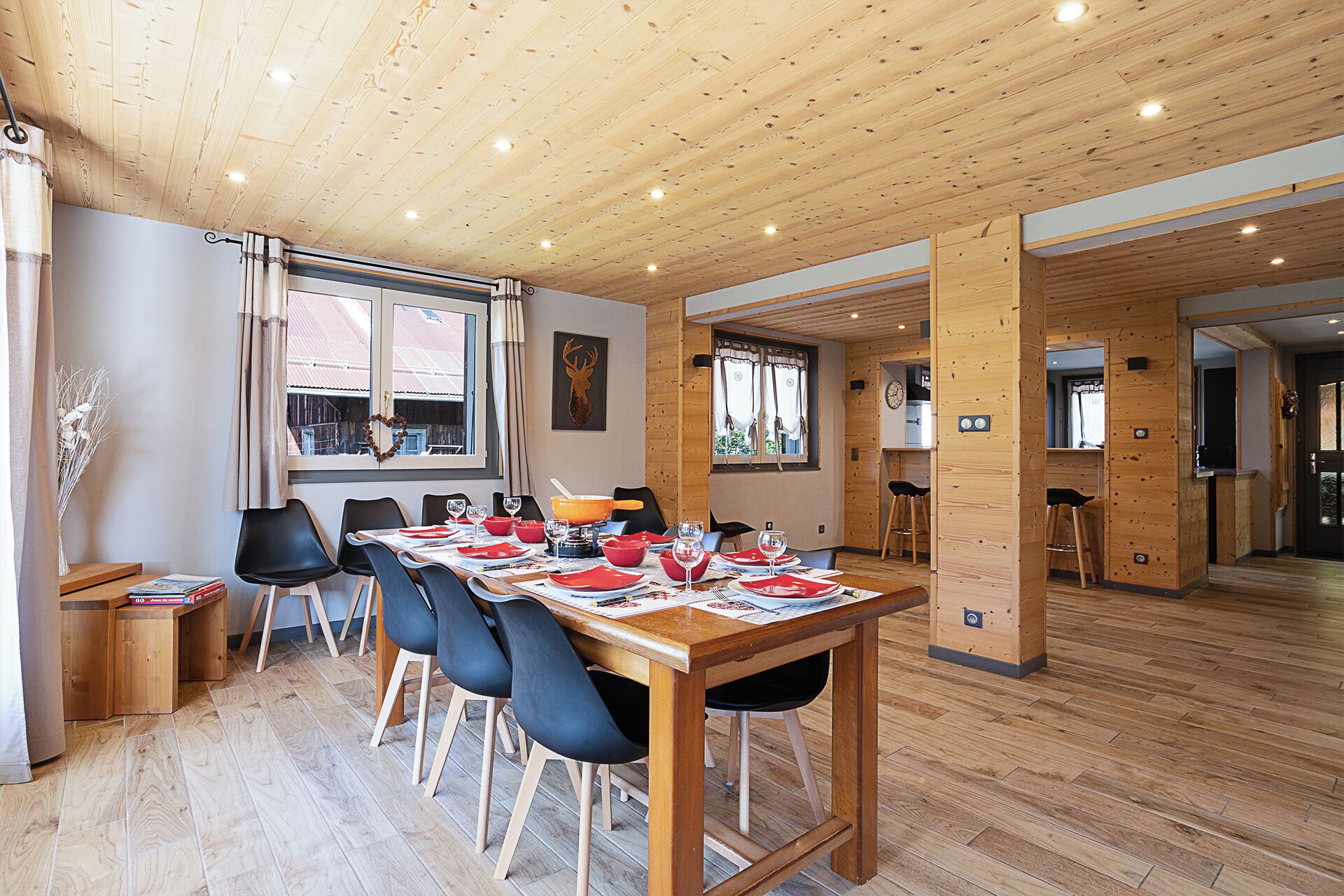 En matplats med ett träbord som är dukat för fyra personer, omgivet av stolar. Det finns fönster med gardiner, en väggklocka och ett trägolv.