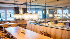 Moderni ravintola, jossa on puupöydät ja -penkit, riippuvalaisimet ja lasiseinä, jossa lukee nimi ”Landgasthof”.