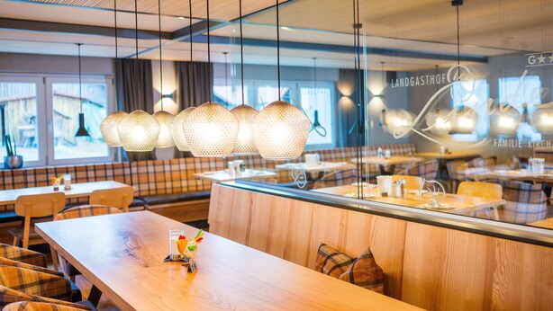 A modern restaurant with wooden tables and benches, hanging pendant lights, and a glass partition with the name "Landgasthof".