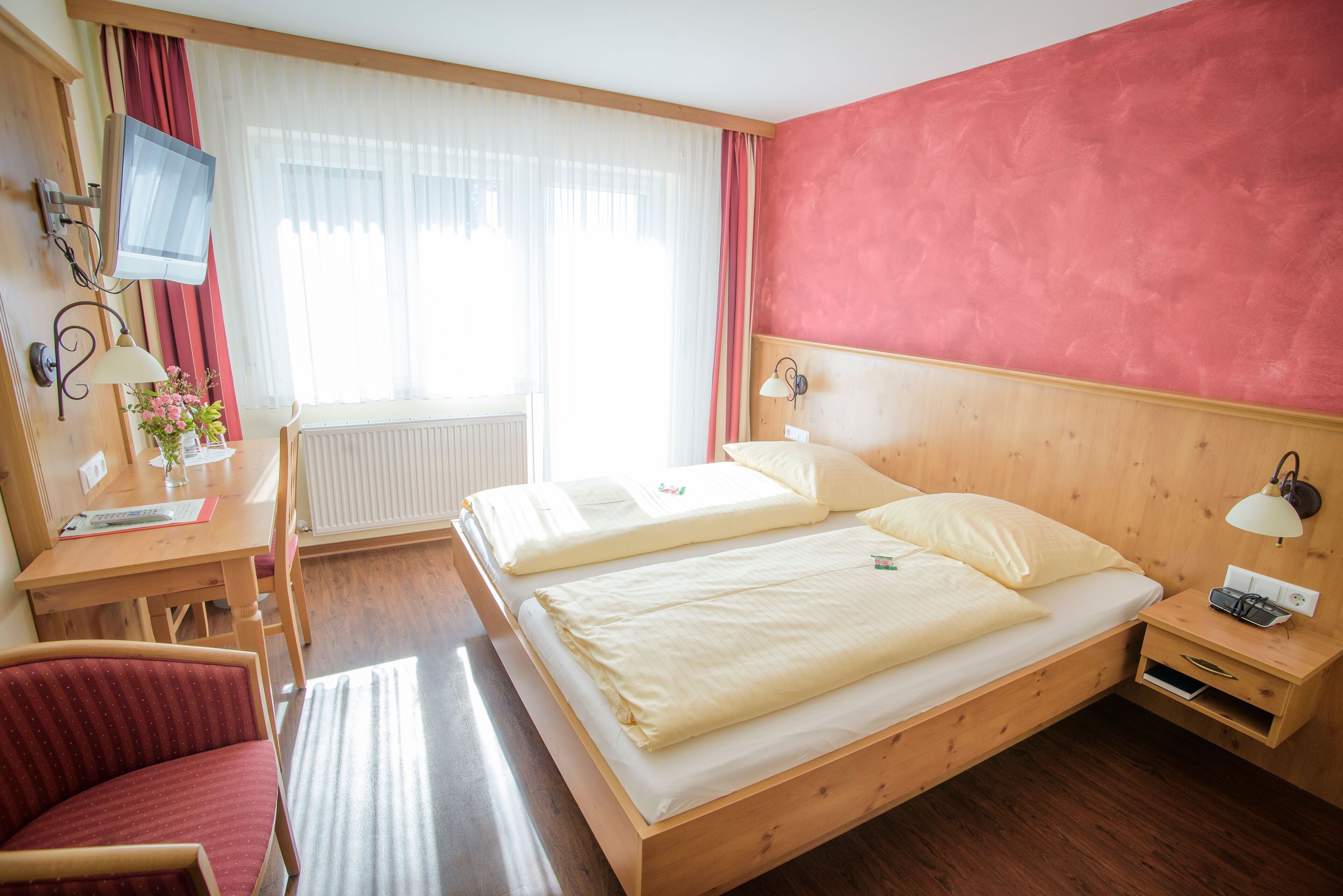 Ein Hotelzimmer mit zwei Betten, einem Schreibtisch, einem Stuhl, einem Fernseher und einem Fenster mit Vorhängen.