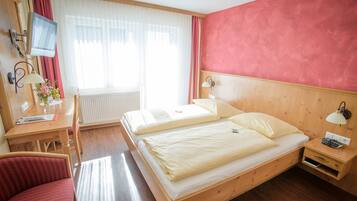 Ein Hotelzimmer mit zwei Betten, einem Schreibtisch, einem Stuhl, einem Fernseher und einem Fenster mit Vorhängen.
