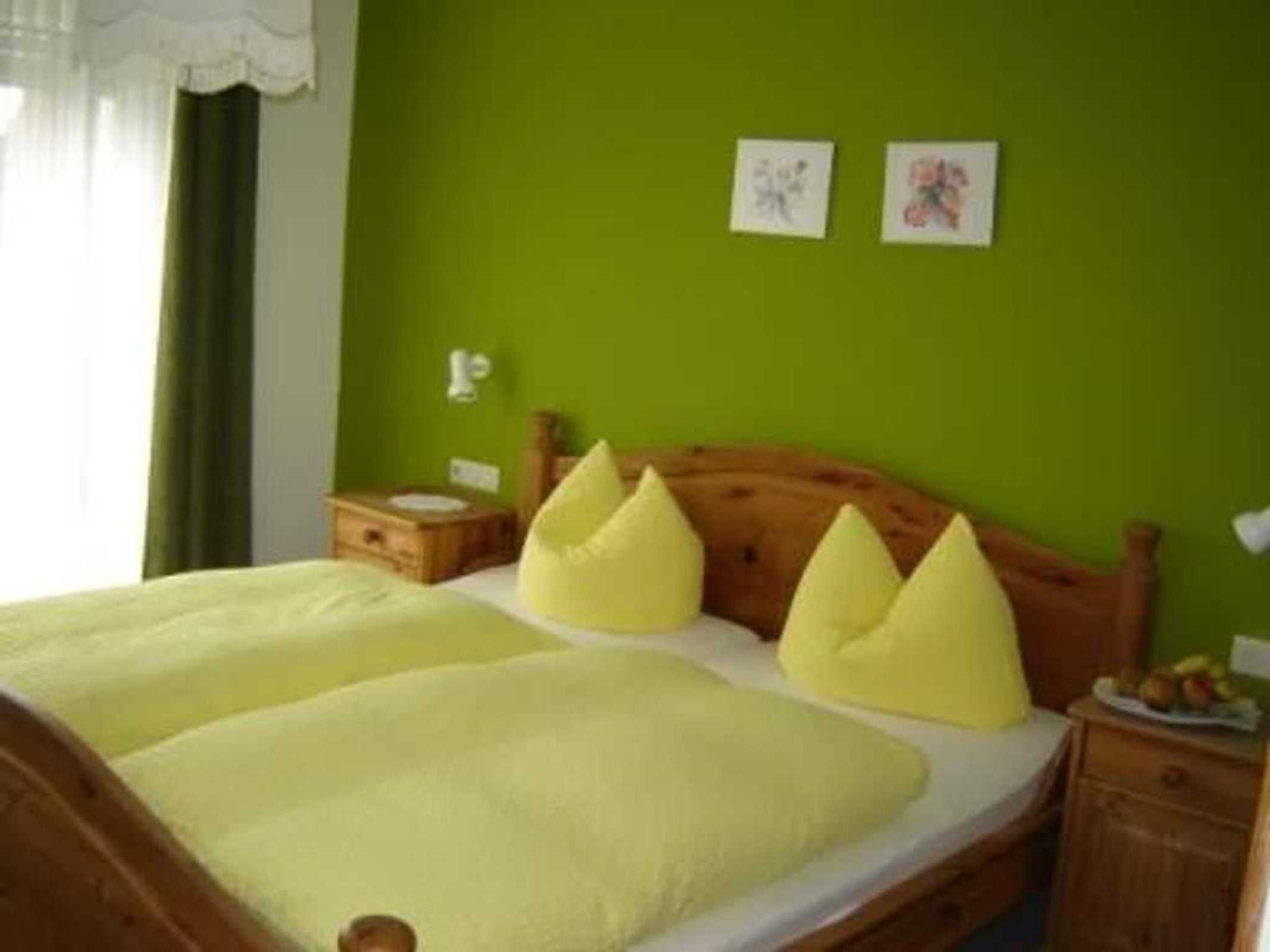 Ein Bett mit hölzernem Kopfteil, einer grünen Wand und zwei kleinen Nachttischen mit Lampen.