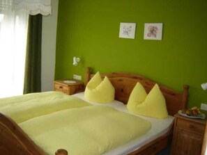 Cama com cabeceira de madeira, parede verde e duas mesinhas de cabeceira com luminárias.