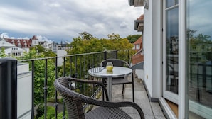 A balcony with wicker furniture and a glass table, overlooking a residential area with houses and trees. - Villa Annabelle Fewo 7 Auszeit - Apartment 7 Auszeit (Binz)