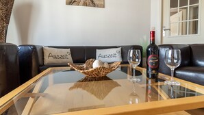 A living room with a glass coffee table, two wine glasses, a bottle of wine, and two cushions with the word "Auszeit" on them. - Villa Annabelle Fewo 7 Auszeit - Apartment 7 Auszeit (Binz)