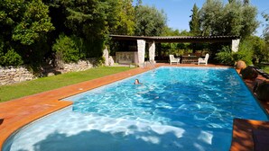 A swimming pool with clear blue water, surrounded by a stone wall and lush greenery. - Casa dos Arrábidos - Turismo em Espaço Rural (Torres Novas)