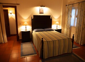 A bedroom with a bed, two bedside tables with lamps, a window with curtains, and a door. - Casa dos Arrábidos - Turismo em Espaço Rural (Torres Novas)