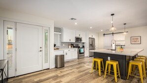 A modern kitchen with white cabinets, stainless steel appliances, a central island with stools, and a 'Good Vibes' sign. - *Heated Pool Available* | South Scottsdale Paradise (Scottsdale)