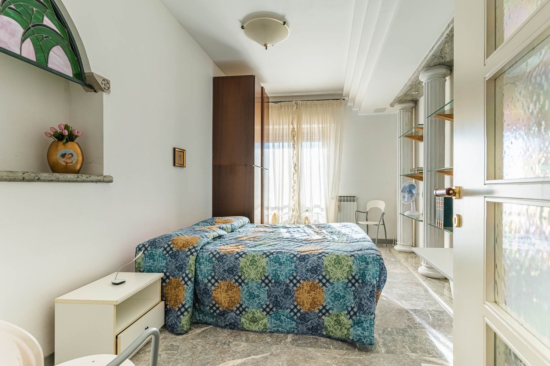 A bedroom with a bed, bedside table, and a window with curtains.