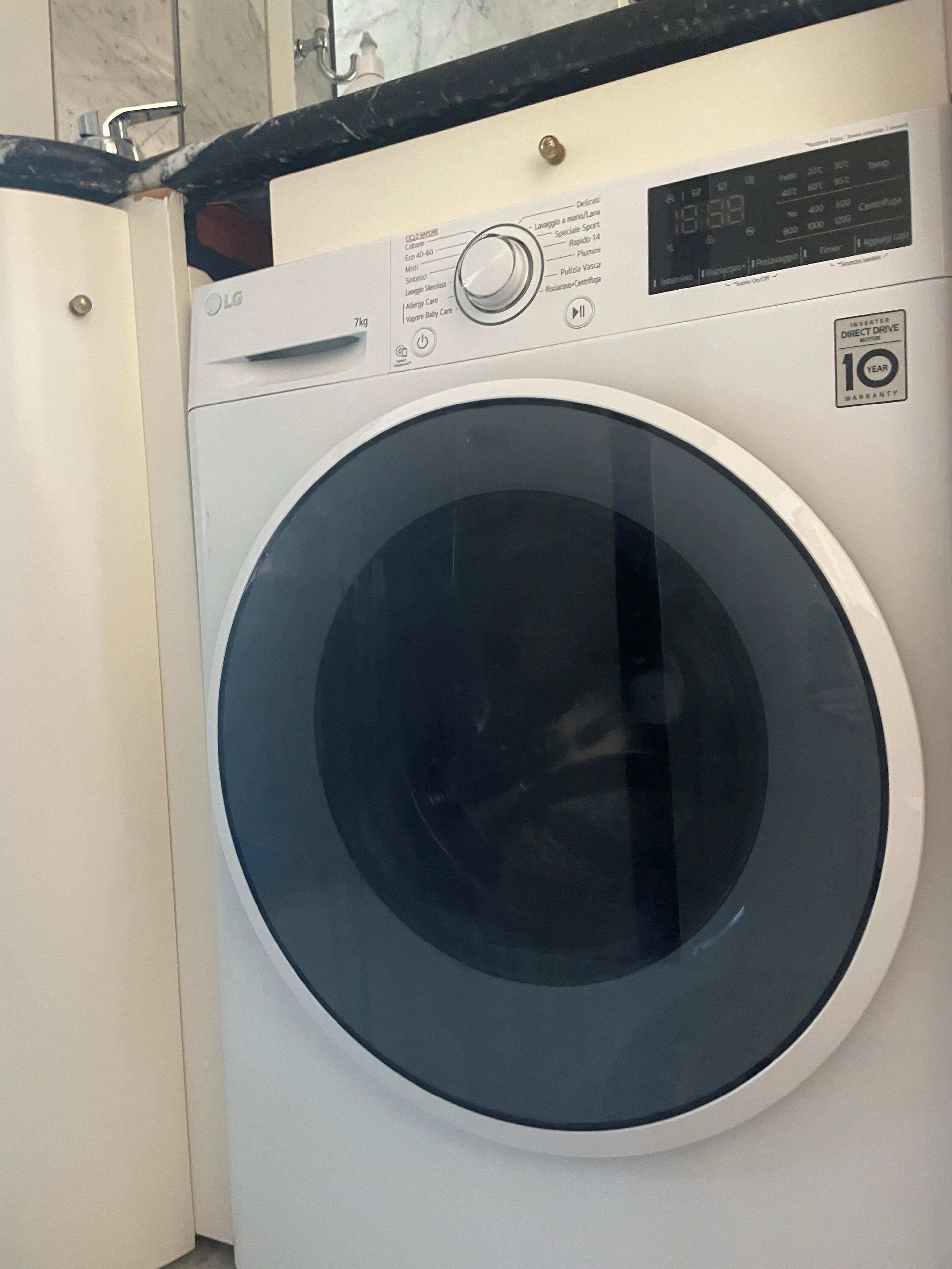 A front view of a white LG washing machine with a digital display, a control panel, and a 10-year warranty sticker.