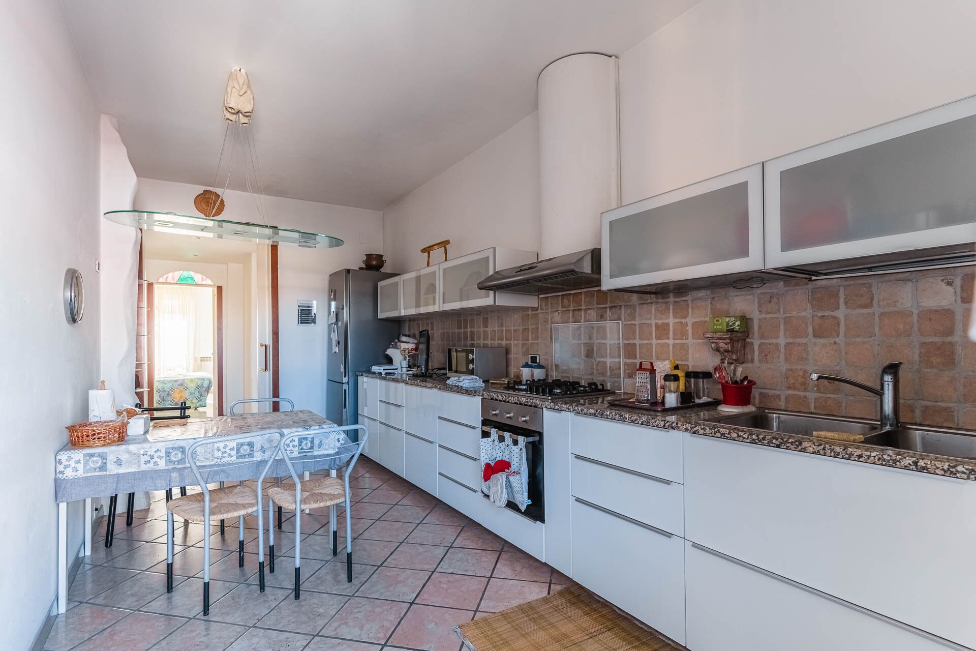 A compact kitchen with white cabinets, a tiled backsplash, and a dining area with a table and chairs.