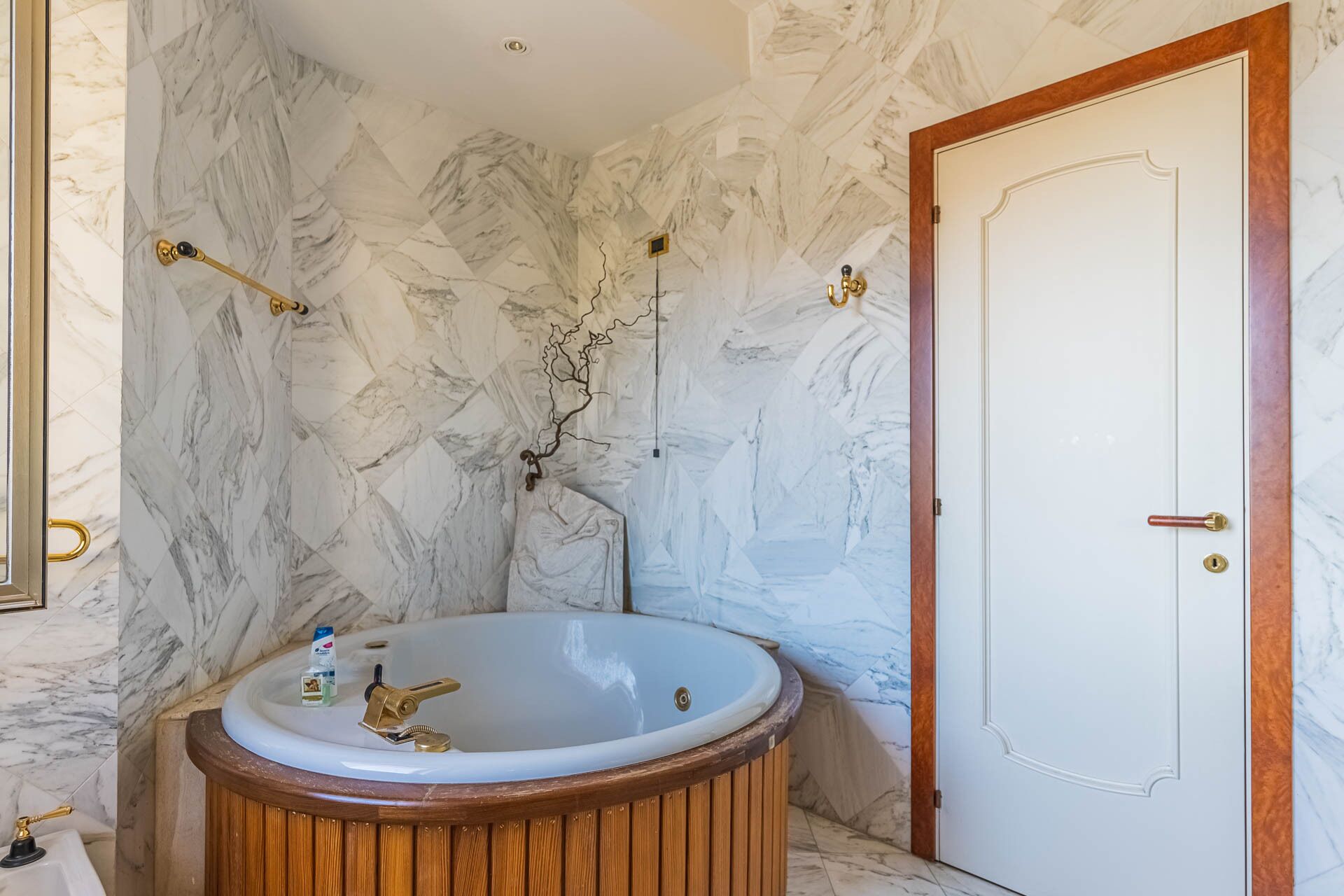A bathroom with a marble wall, a wooden bathtub, and a white door.