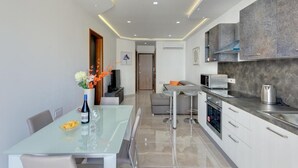 Une cuisine moderne avec une table à manger en verre, des meubles de rangement gris et un four encastré.