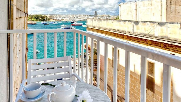 Un balcon avec une table préparée pour le thé, donnant sur un port où sont amarrés des bateaux.