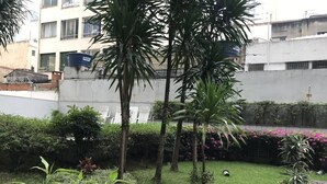 A courtyard with potted plants, a grassy area, and a building with a sign that reads "FORTY". - Apto Conforto C/ Netflix Amazon Prime Disponível (SP)