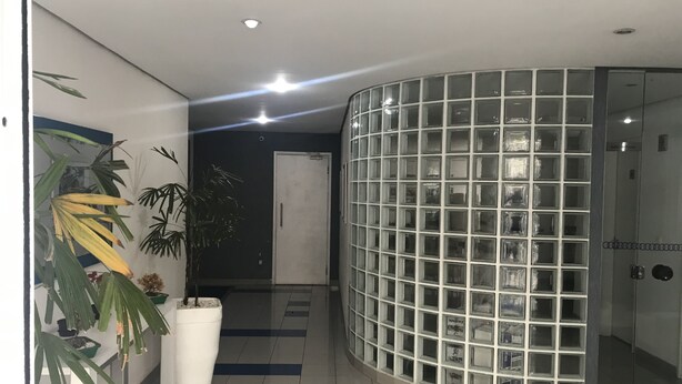 A modern hallway with a curved glass wall, a white door, and potted plants. - Apto Conforto C/ Netflix Amazon Prime Disponível (SP)