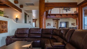 A spacious living room with a large leather sectional sofa, wooden coffee table, and a high wooden ceiling with exposed beams.
