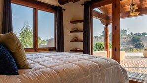 A bedroom with a large bed, wooden beams, a view of the outdoors, and a balcony.