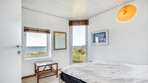 A bedroom with a bed, a small wooden table, two windows with views of the sea, and a wall-mounted light fixture. - 6 bedroom gorgeous home in Gilleleje (Gilleleje)