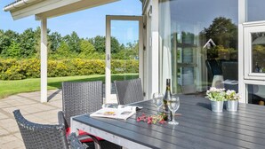 Et udendørs spiseområde med et bord, stole og en flaske vin.