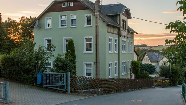 Ein zweistöckiges Gebäude mit geneigtem Dach, zahlreichen Fenstern und einer Satellitenschüssel.