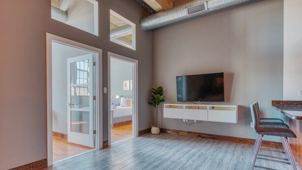 Una sala moderna con un televisor de pantalla plana, un mueble blanco para entretenimiento, una planta en maceta y una zona de bar con taburetes.