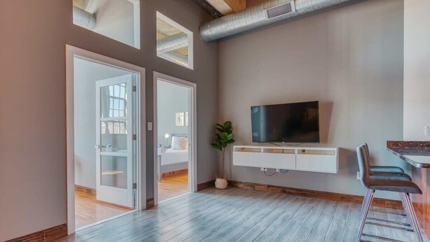 A modern living room with a TV, bar area, and a sliding door leading to another room. - Sosuite | 2BR Apt w W/D, Gym, On-Site Restaurant (Philadelphia)