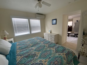 A bedroom with a bed, dresser, and a view of the kitchen.