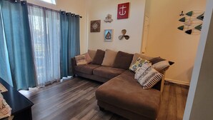 A living room with a brown sofa, a small table, and a window with blue curtains.