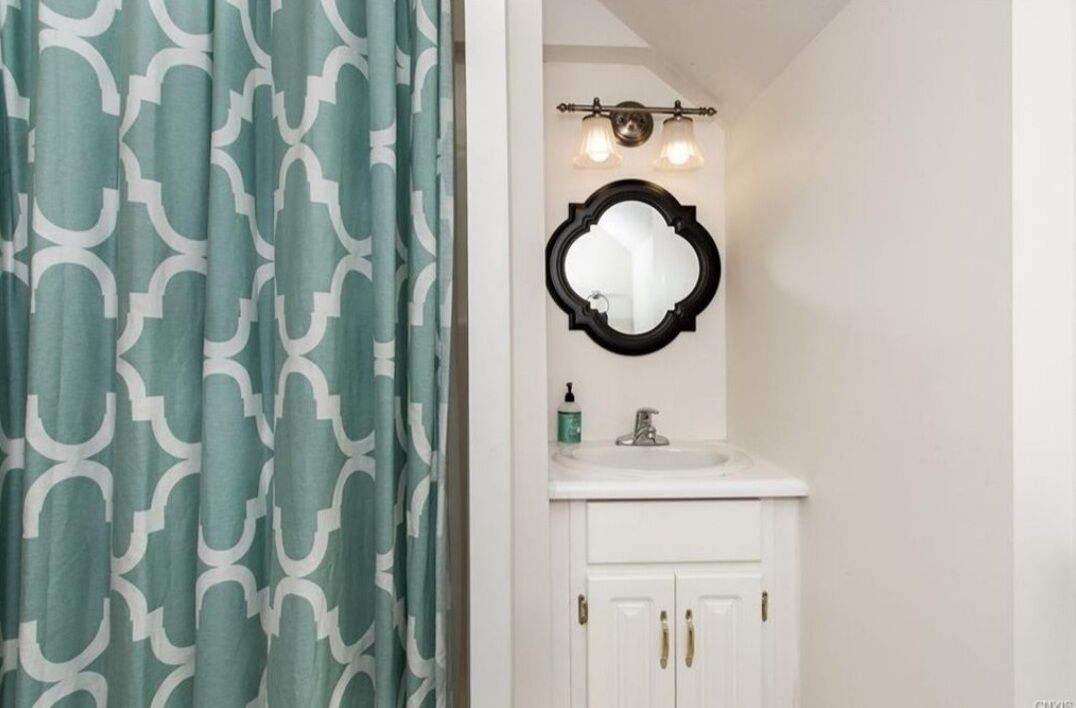 A bathroom with a white sink, a mirror, and a green patterned shower curtain.