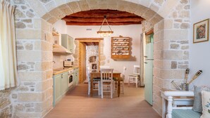 A rustic kitchen with stone walls, wooden beams, a dining area with white chairs, and a small table. - Joakim's villa  (herakleion)