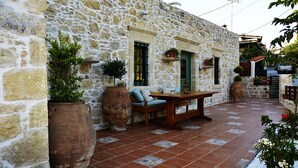 A stone building with a patio area featuring a wooden table and chairs, large planters, and a tiled floor. - Joakim's villa  (herakleion)