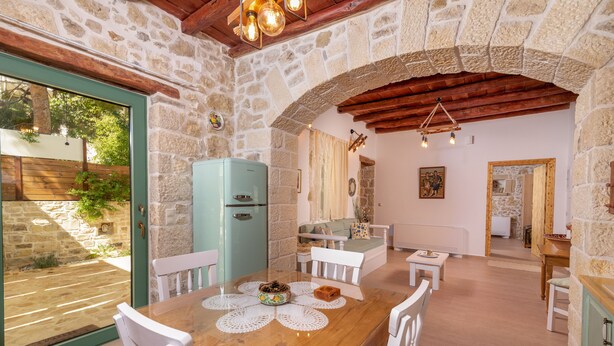 A rustic dining area with a wooden table, white chairs, and a stone wall backdrop. - Joakim's villa  (herakleion)
