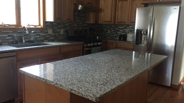 A kitchen with granite countertops, wooden cabinets, a stainless steel refrigerator, and a microwave. - Welcome to the Adirondacks (Boonville)