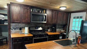 A kitchen with dark wood cabinets, a stainless steel microwave, a gas stove, and a wooden countertop.