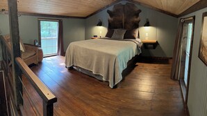 A bedroom with a large bed, wooden flooring, a sloped ceiling, and a rustic decor.