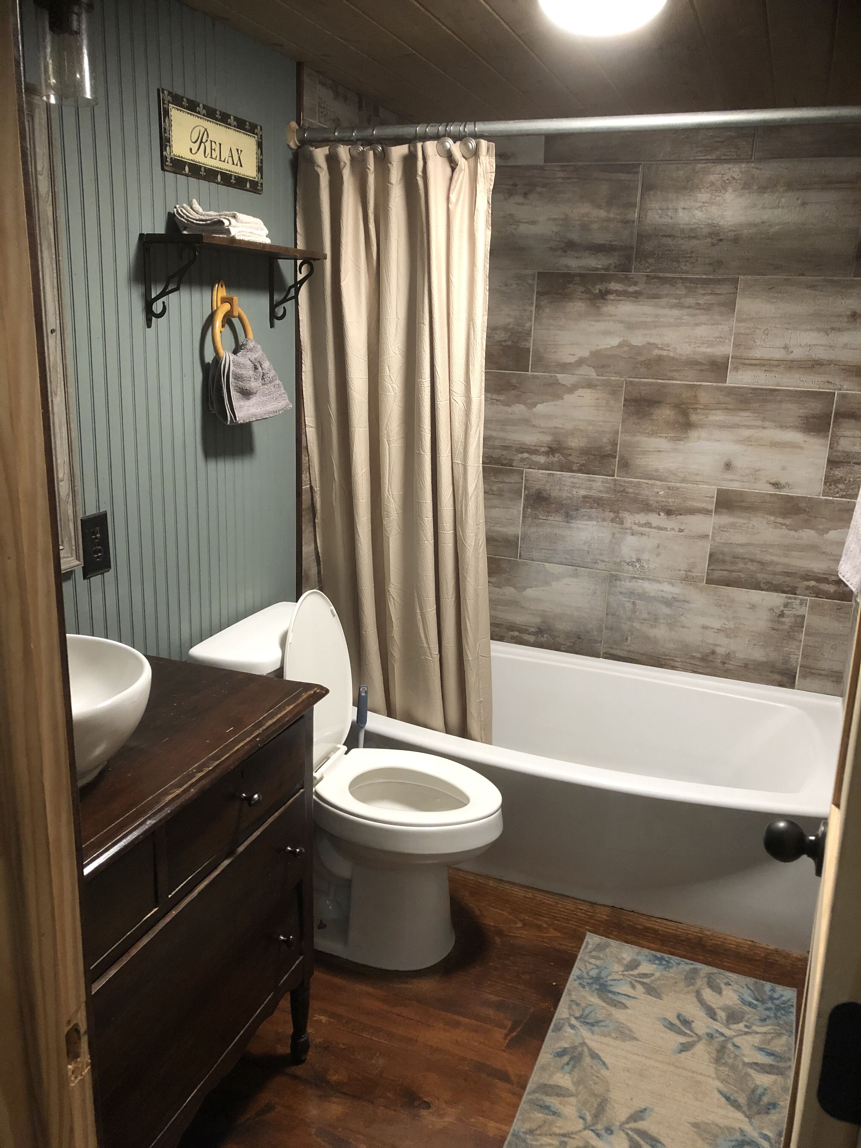 A bathroom with a wooden vanity, a toilet, a bathtub, and a shower curtain.