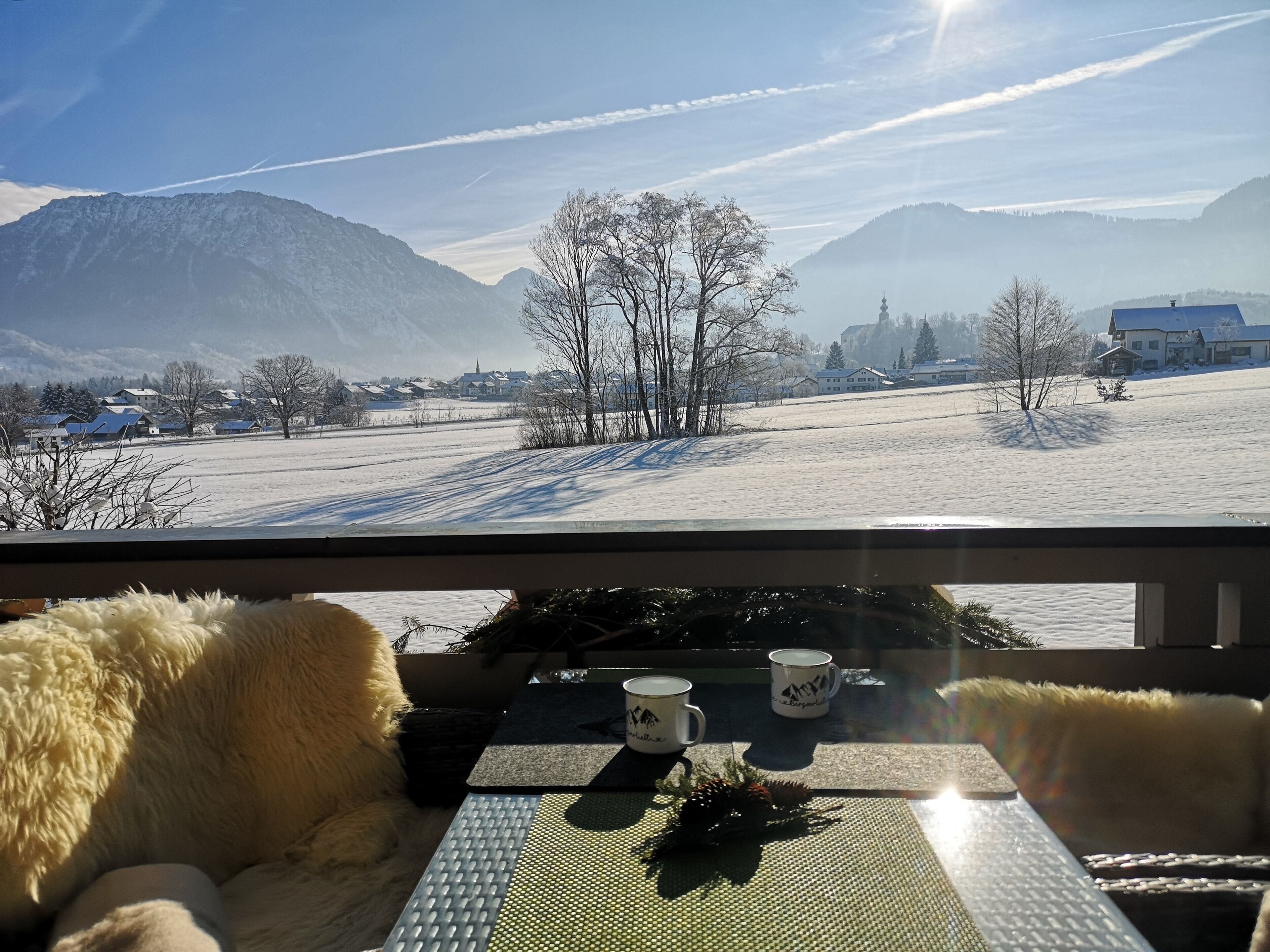 Una habitación con vistas a un paisaje nevado, una mesa con dos tazas y un almohadón blanco y mullido.