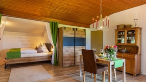 Ein gemütliches Zimmer mit Holzboden, einem Bett mit grünen Vorhängen, einem Esstisch mit Stühlen und einem Schrank mit Körben.