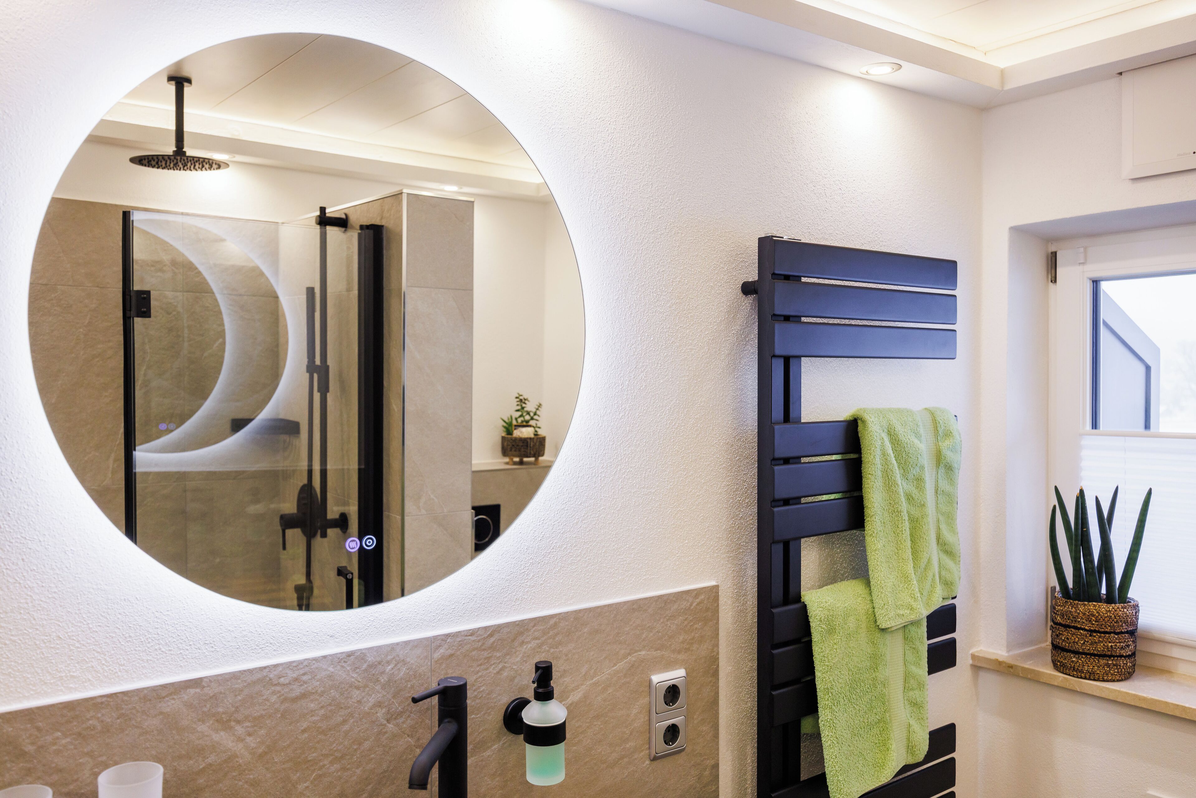 A bathroom with a circular mirror, a towel rack, a potted plant, and a shower area.