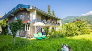 Ein zweistöckiges Haus mit Balkon, einem kleinen Baum und einer Katze im Gras.