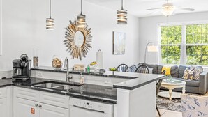 Una cocina moderna con una isla central, luces colgantes y una zona de comedor con sofá y mesa de centro.