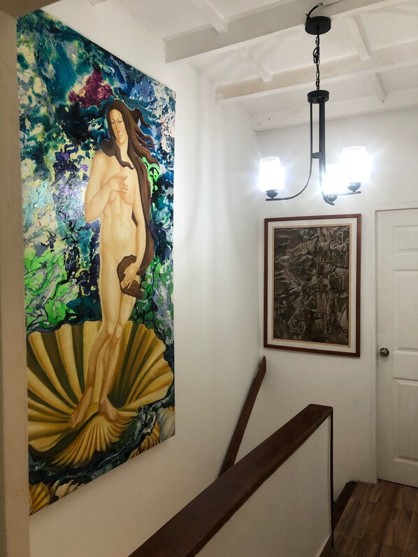 Un escalier avec une rampe en bois, un grand tableau abstrait, une œuvre d’art encadrée et un lustre.