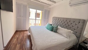 A bedroom with a large bed, a wooden floor, a ceiling with exposed beams, and a window with a view of the outside. - Hermoso Duplex Bovedas (Cartagena)