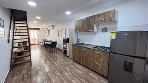 A modern kitchen with wooden cabinets, a stainless steel refrigerator, and a dining area with a table and chairs. - Hermoso Duplex Bovedas (Cartagena)